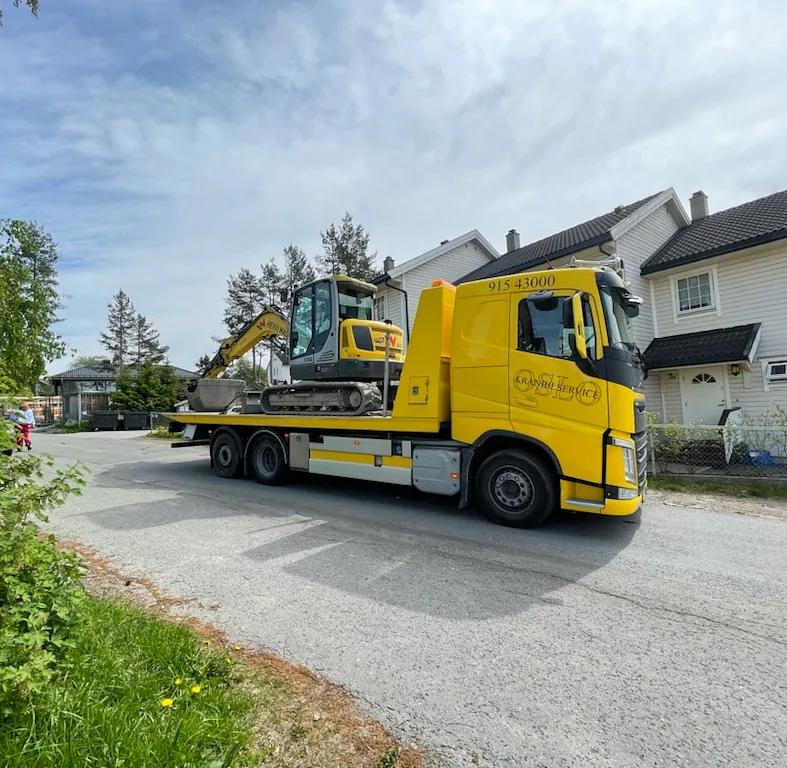 Gul lastebil med gravemaskin parkert foran bolig