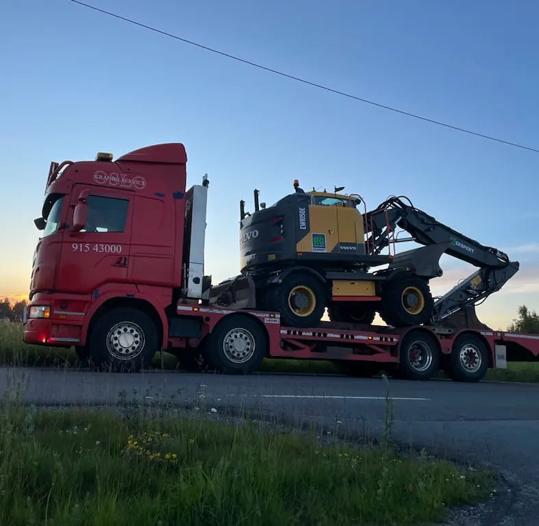 Rød lastebil som frakter gul gravemaskin