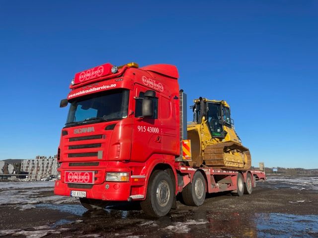 Rød lastebil som frakter gul arbeidskjøretøy